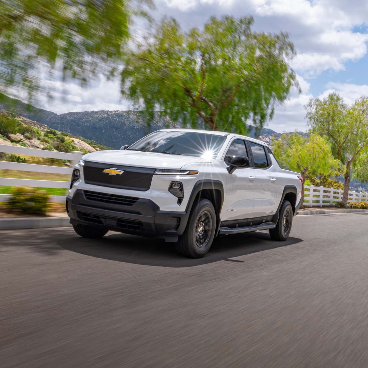 A GM Envolve vehicle driving by a hillside road on a sunny day.