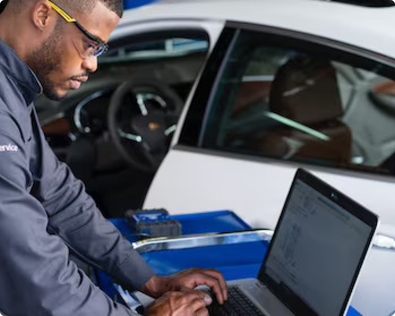 A Certified Service Technician using a laptop beside a GM Fleet vehicle.