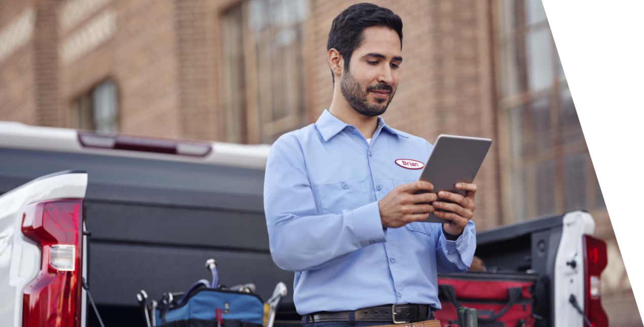 A GM Envolve personnel using a tablet beside a GM vehicle.