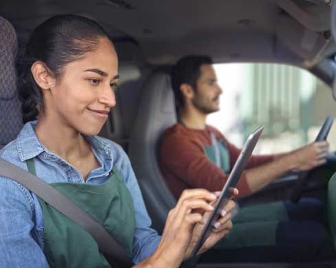 Two People Sitting in a Car with the Passenger Looking at a Tablet.