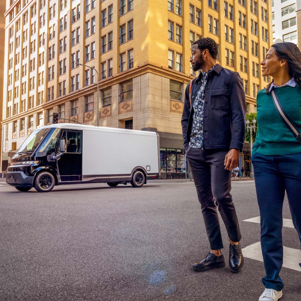 A Couple Walking by a BrightDrop Zevo Driving Down the City Street