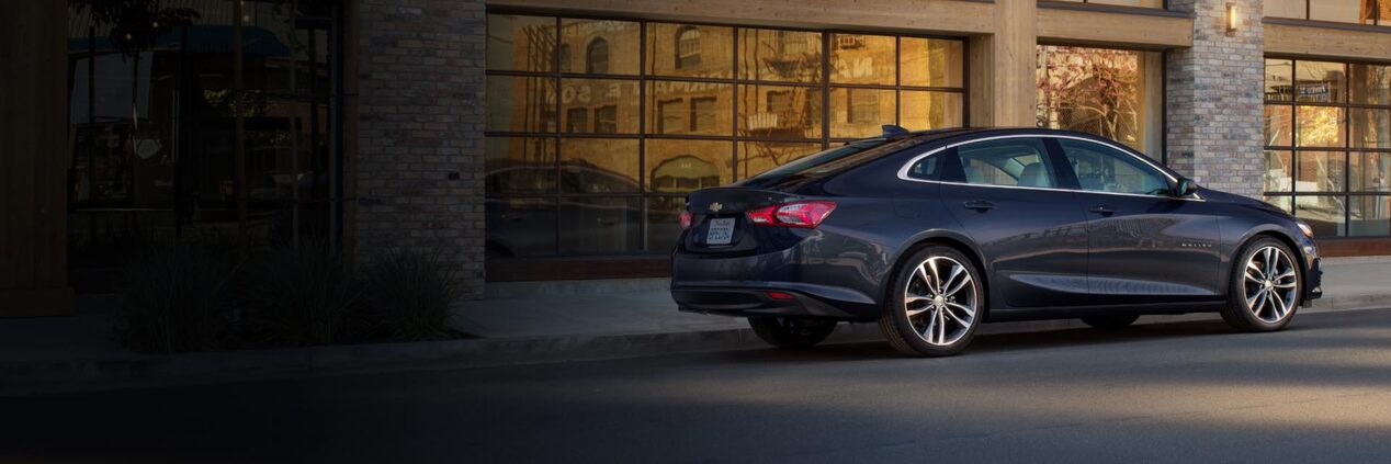 Rear Three-Quarters View of the 2024 Chevrolet Malibu Parked In Front of a Building