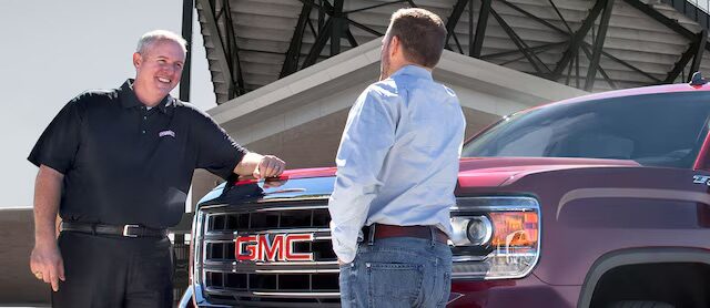 two people talking in front of a GMC vehicle