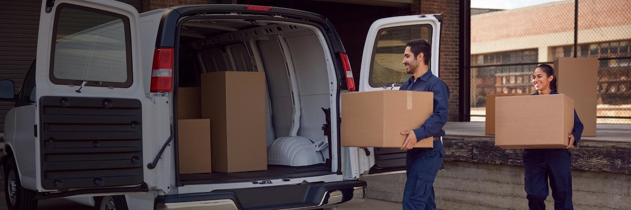 Two People Carry Cardboard Boxes Towards an Open Rear Door of a Fleet Van