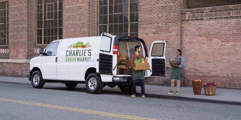 Two People Unloading Produce from a Cargo Van Next to a Business