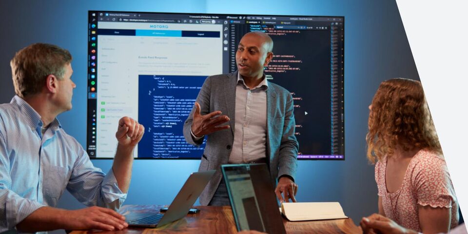 Three People Having a Discussion with a Screen in the Background Showing Website Mockups and Code