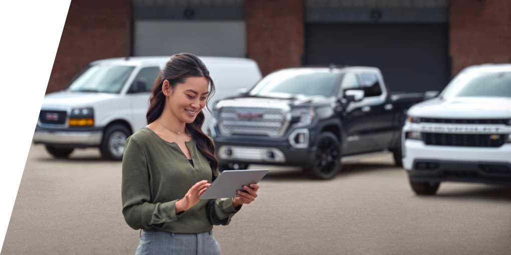 A Woman Standing in a Parking Lot Looking at a Tablet With Vehicles in the Background