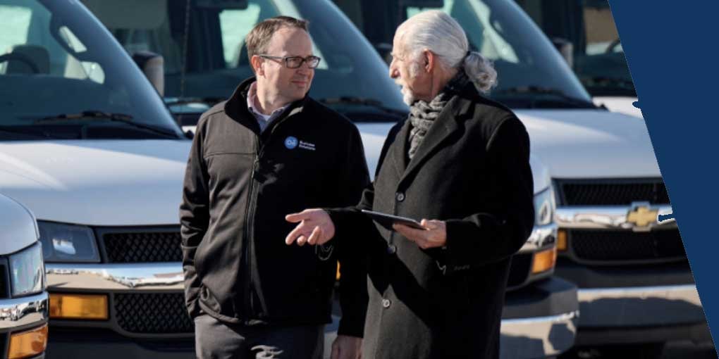 Two People Walking Side by Side Having a Conversation with Vehicles in the Background