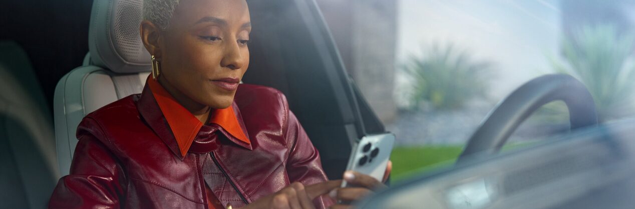 A person seated at a driver's seat using a smartphone to access the OnStar mobile app.