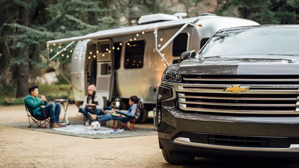 A car in front of a trailer that has been set up for camping.