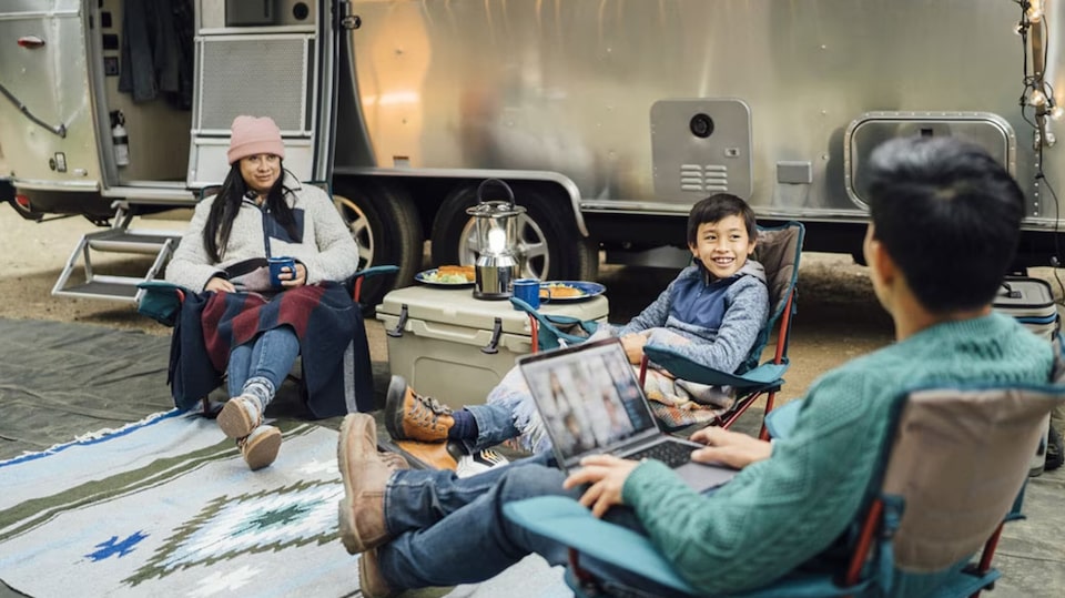 A family gathered together in front of their trailer set up for camping.