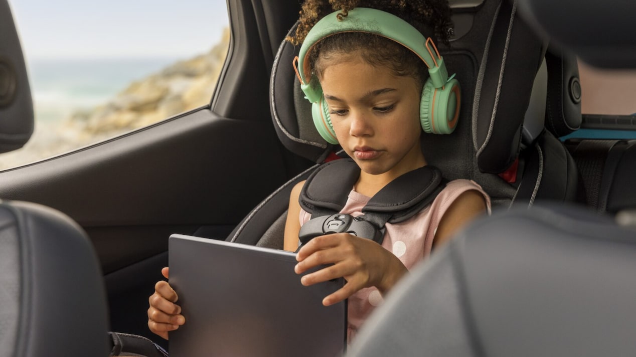 Child using various gadgets comfortably while riding in car.