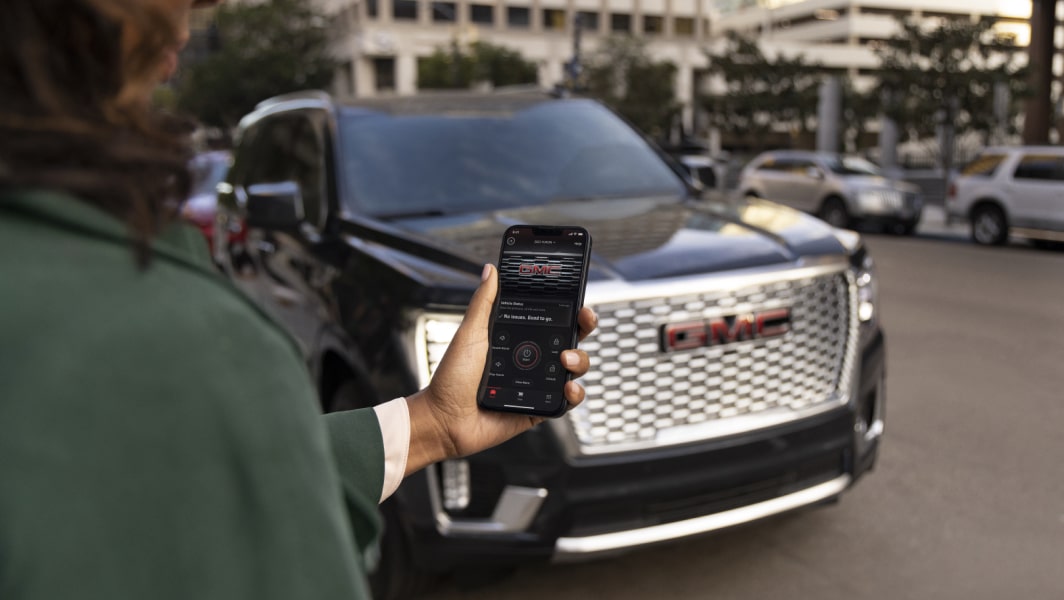 A person accessing an OnStar feature on a smartphone outside a GMC vehicle.