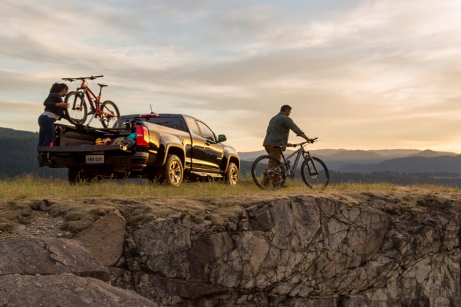 Two people getting their bicycles from their truck in a cliff area.